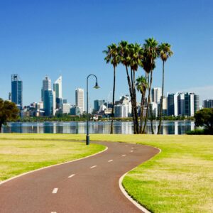 Vibrant Perth skyline with palm trees and curved pathway reflecting on Swan River under a clear blue sky.