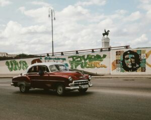 Classic Chevrolet car cruising past Havana street art with Che Guevara mural.