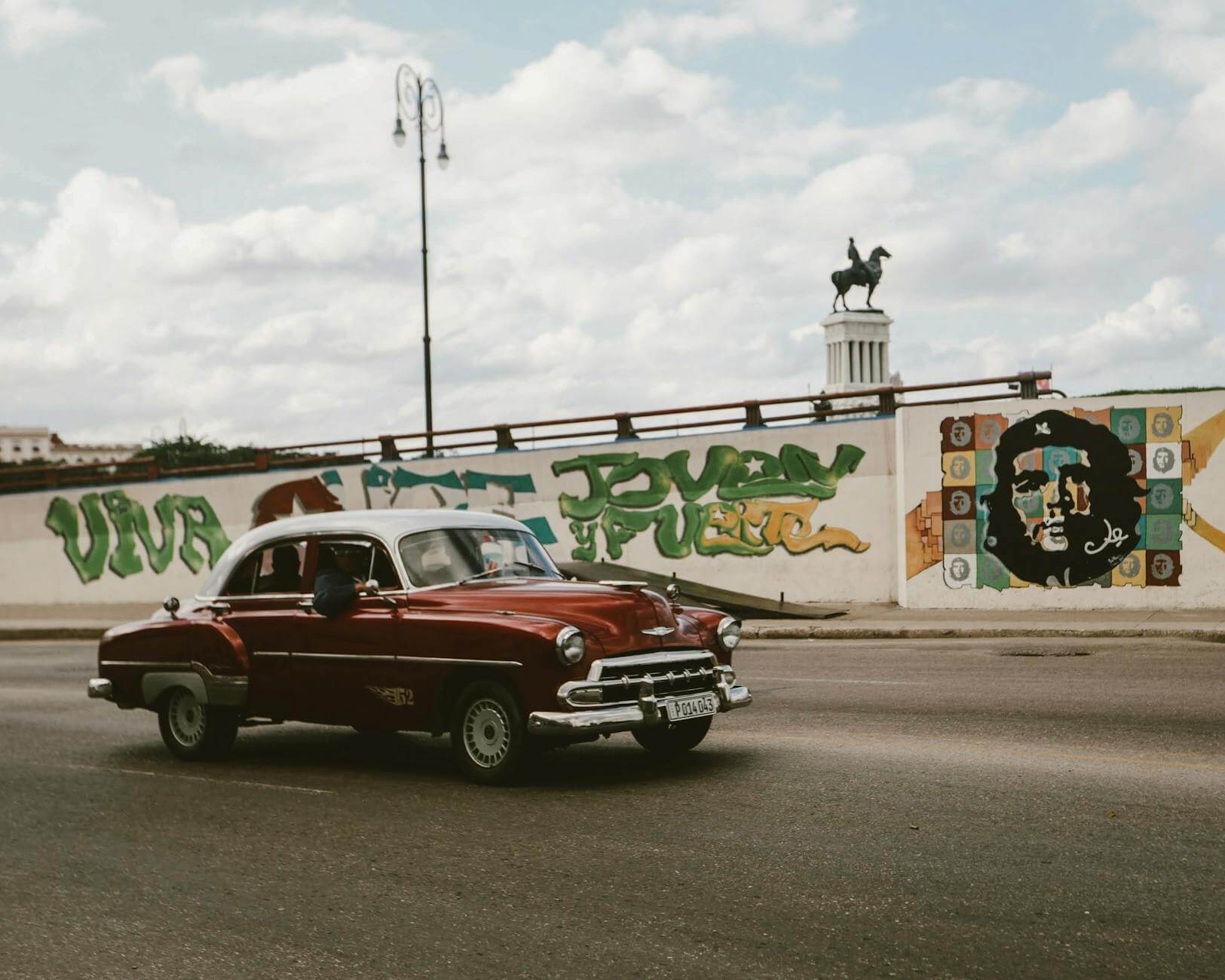 Classic Chevrolet car cruising past Havana street art with Che Guevara mural.