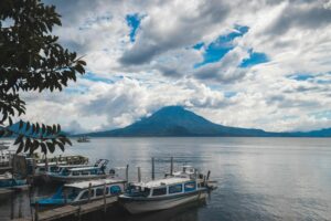 Boats docked with a stunning view of Lake Atitlan and its volcano under a cloudy sky.